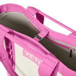 Close-up of a bright pink and off-white YETI Camino Carryall 35 bag, revealing its open top, the embossed pink YETI logo, an interior zippered pocket, and a central black buckle