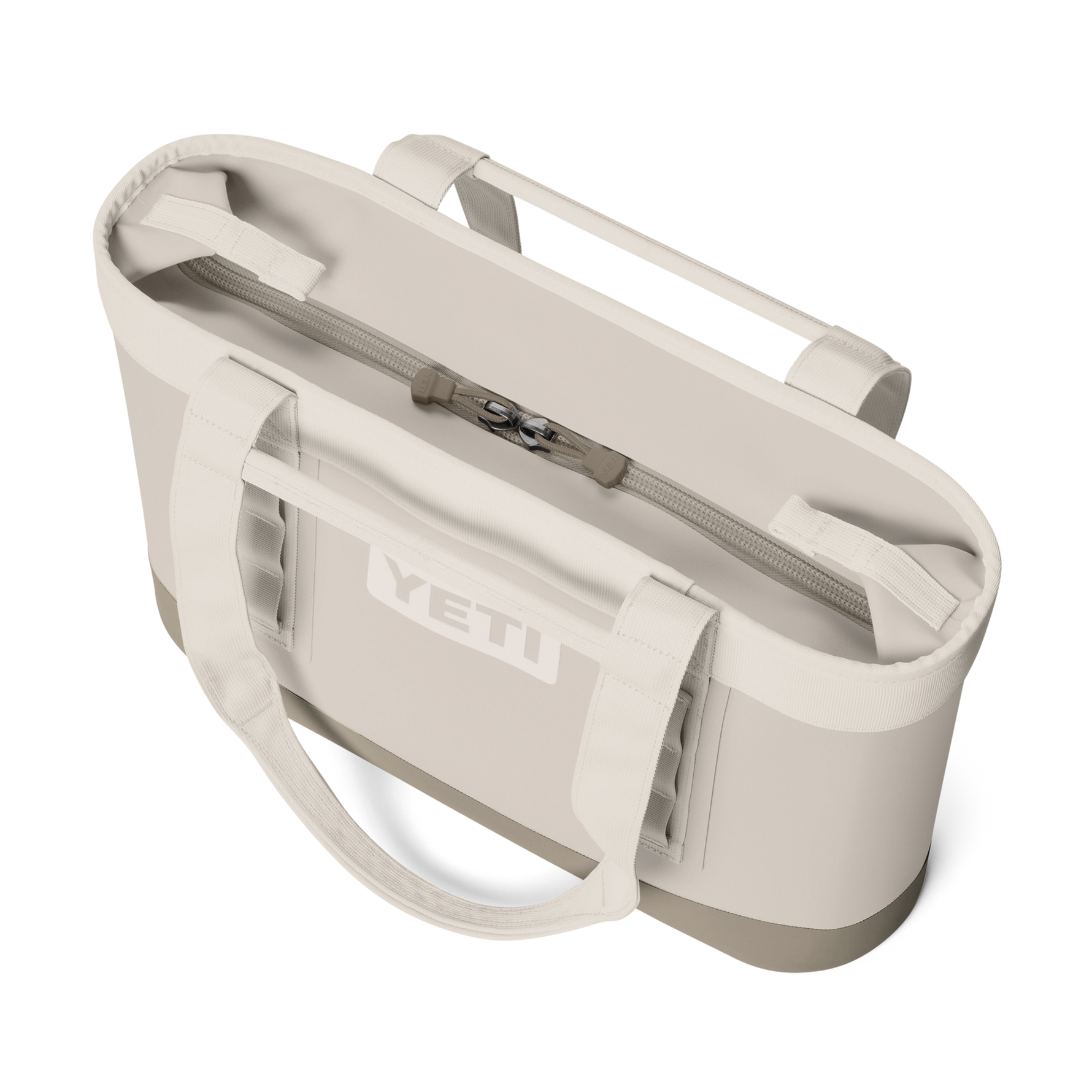 Product photograph of a YETI Camino Carryall tote bag on a black background featuring a cream-colored waterproof shell, the prominent white YETI logo, and a zippered top closure with reinforced straps and utility loops