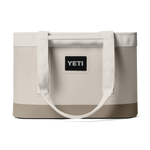 Product photography by YETI of a cream-colored Camino Carryall tote bag featuring a reinforced taupe base, thick woven shoulder straps, and a prominent black logo patch centered on the front against a dark background