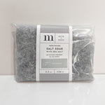 A clear plastic bag of m BATH + BODY Soothing Salt Soak with Sea Salt, filled with small grey crystalline salts and featuring a white label with No 27 Cashmere scent details and black and white polka dot accents