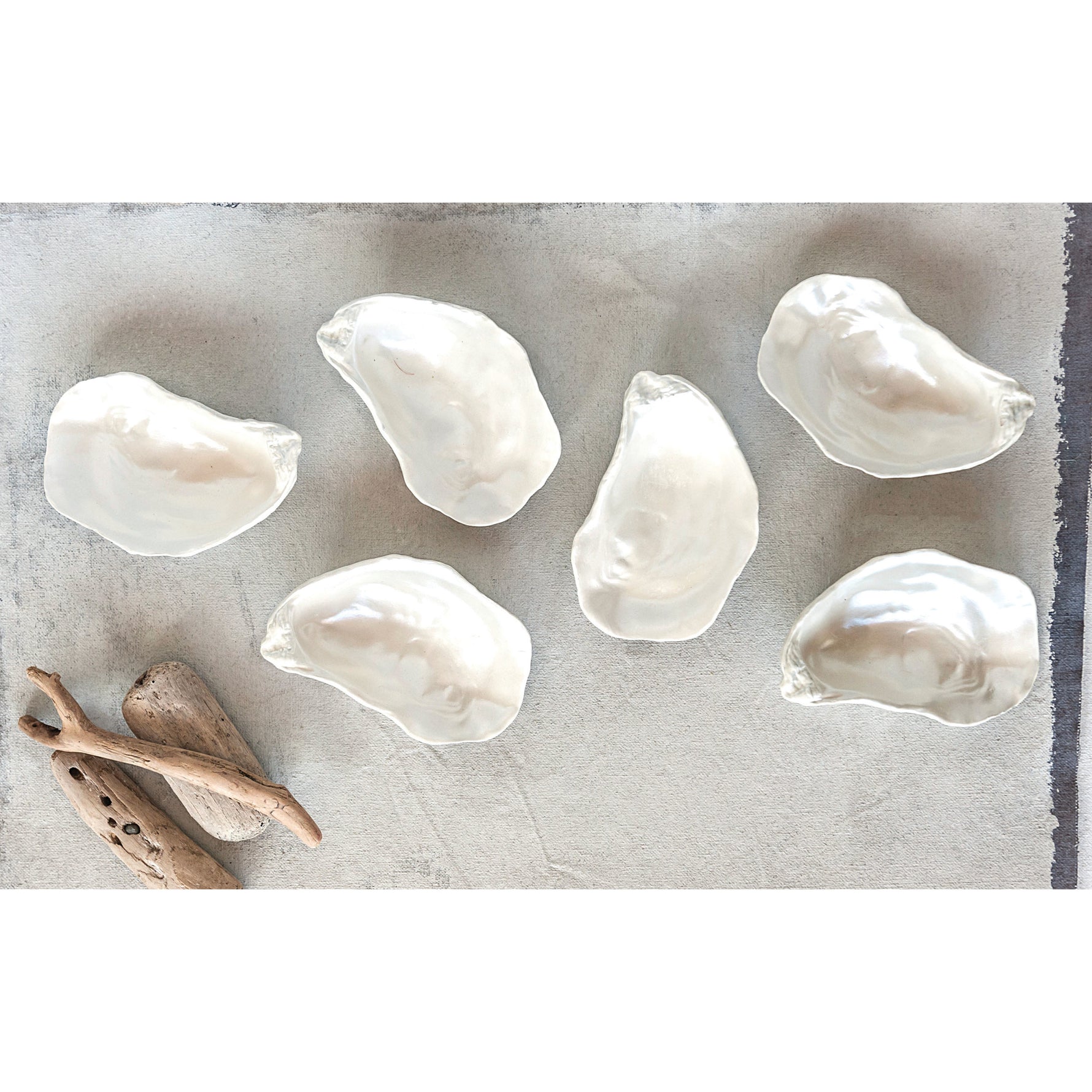 Five white ceramic oyster shells arranged on a grey textured surface with pieces of driftwood