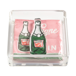 Clear acrylic napkin holder displaying pink cocktail napkins with illustrated green champagne bottles and "Champagne" labels