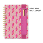 Spiral-bound planner with a light pink speckled cover patterned with fuchsia lightning bolts, featuring gold spiral binding and a magenta elastic band pen loop holding a gold pen that is not included