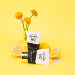 Product photograph featuring two Chez Gagné Oh Heel No Foot Creme tubes on a vibrant yellow background with sliced lemons, yellow globe flowers in a clear vase, and white sea salt crystals