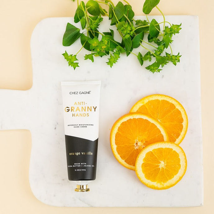Tube of orange vanilla hand cream with orange slices and green herbs on a marble board