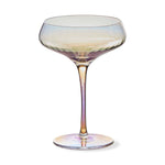 Iridescent glass champagne coupe glass featuring a wide bowl with subtle ripple texture, a long stem, and a round base reflecting shifting hues of pink, purple, yellow, and blue