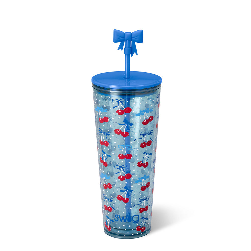 Plastic reusable tumbler by Swig Life on a white background featuring a red cherry and blue ribbon pattern, a solid blue lid, and a unique three-dimensional blue bow straw topper