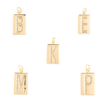 Jewelry design featuring five gold-toned rectangular alphabet pendants with pavé crystal initials B, E, K, M, and P on a white studio background with polished metallic finishes and top hanging bails