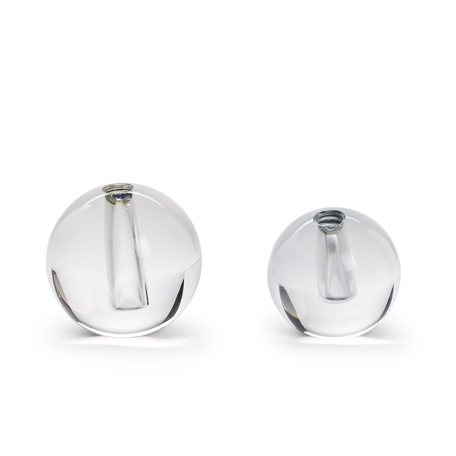 Clear glass, a duo of polished spherical vases in two sizes, each precisely crafted with a narrow internal tube for a single flower stem, against a stark white background