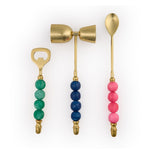 Product Photography three gold cocktail bar tools a bottle opener with a green beaded handle a double jigger with a blue beaded handle and a mixing spoon with a pink beaded handle