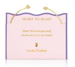 Lucky Feather product photo of a gold-tone Heart to Heart open cuff bracelet with small heart ends displayed on a pink and lavender card featuring the golden text HEART TO HEART and the message Wear this bracelet and know you're in my heart