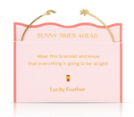 Gold bracelet by Lucky Feather, featuring wave and sun charms, presented on a pale pink card with a coral wavy border, gold text 'Sunny Skies Ahead', and a small golden feather charm