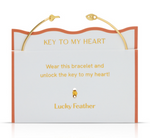 Product image by Lucky Feather of a gold cuff bracelet with key ends presented on a white and orange "KEY TO MY HEART" display card