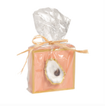 Square pink wooden block with gold trim and oyster shell ornament wrapped in clear plastic with raffia bow
