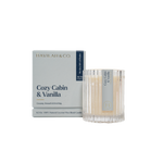 Product photography by Havilah & Co featuring a Cozy Cabin & Vanilla scented candle in a ribbed glass jar and its minimalist light blue box on a black backdrop with elegant gold foil typography and a navy blue 50/50 Company seal