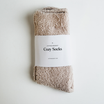 Studio photograph by Gifted Market showing plush taupe Cozy Socks secured with a white branded paper band on a minimalist white surface