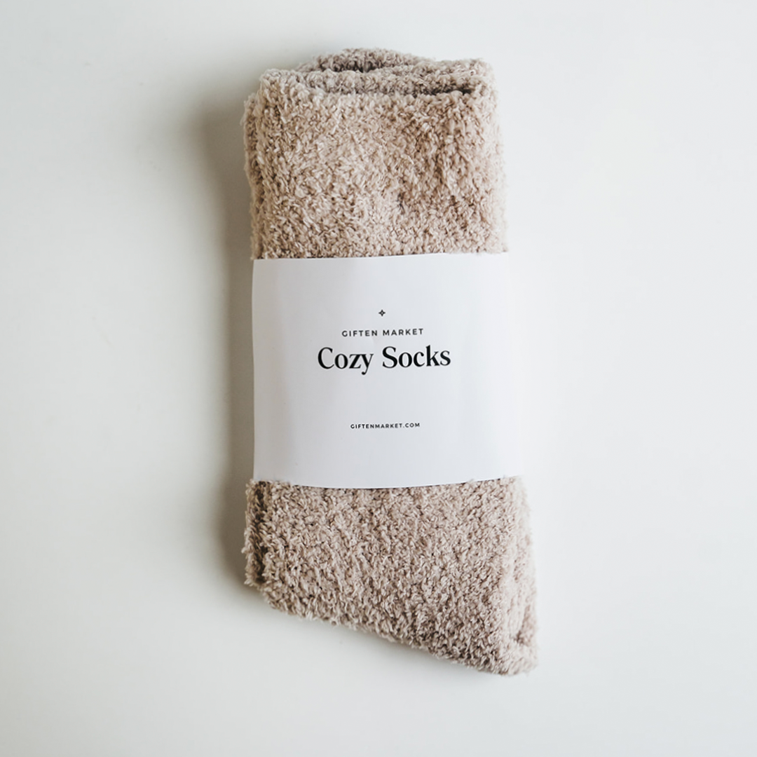 Studio photograph by Gifted Market showing plush taupe Cozy Socks secured with a white branded paper band on a minimalist white surface