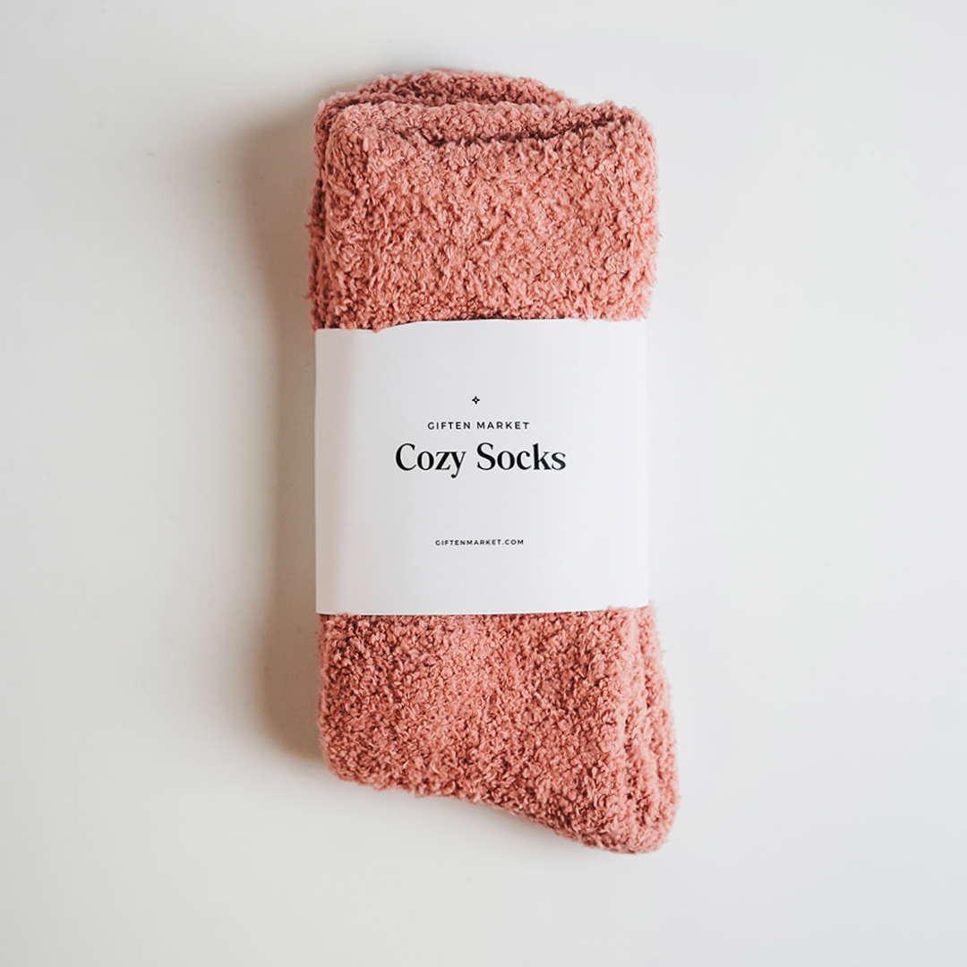 Photograph of dusty rose fluffy GIFTEN MARKET Cozy Socks featuring a white paper band label with "Cozy Socks" text on a minimalist white background