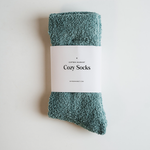 Product photography of Gifted Market seafoam green cozy socks with a fluffy texture and a white label displaying "Cozy Socks" on a clean white background