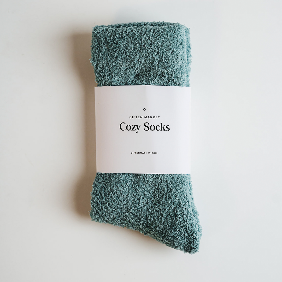 Product photography of Gifted Market seafoam green cozy socks with a fluffy texture and a white label displaying "Cozy Socks" on a clean white background