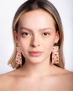 Woman on a white background wearing fringe earrings.