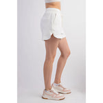 Studio product shot of a person modeling white drawstring athletic shorts featuring side pockets and a curved hem, paired with pink and beige retro-style sneakers with white laces