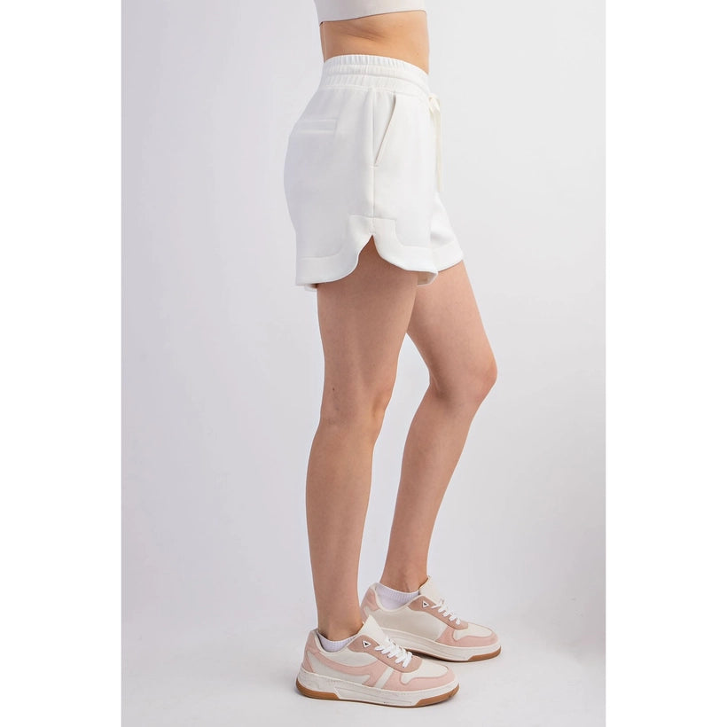 Studio product shot of a person modeling white drawstring athletic shorts featuring side pockets and a curved hem, paired with pink and beige retro-style sneakers with white laces