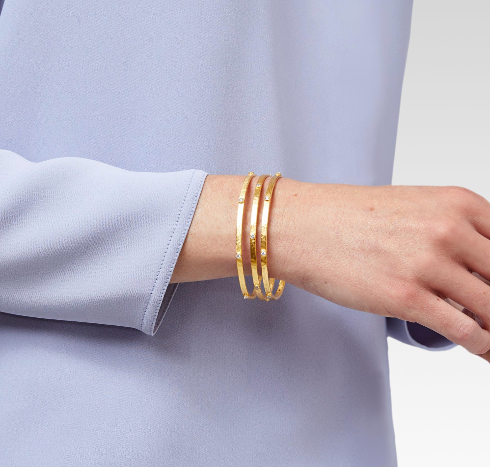 Three gold hammered bangles with small inset diamonds worn on a wrist