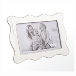 White enamel and silver scalloped photo frame with a prominent silver cross in the top left corner holding a black and white image of three laughing children