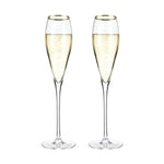 Two elegant champagne flutes filled with golden bubbling champagne featuring distinctive gold rims and tall clear stems on a bright white background