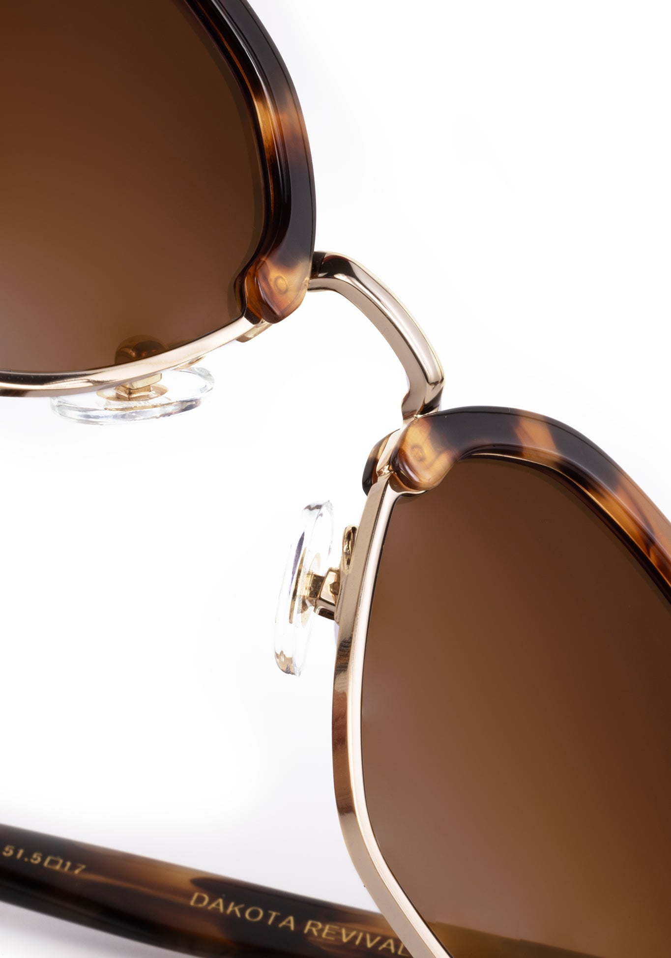 Digital photograph by DAKOTA REVIVAL a close-up of tortoiseshell sunglasses with brown tinted lenses gold metal frames clear nose pads and the DAKOTA REVIVAL brand name visible on the temple against a white background