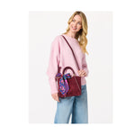 Woman wearing a pink sweater and blue jeans holding a burgundy handbag with a floral scarf tied to the handle