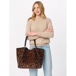 Woman holding a large leopard print tote bag with black leather handles
