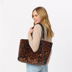 Woman carrying a leopard print tote bag with black leather handles over her shoulder