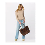 Woman wearing beige sweater and light blue jeans holding a leopard print tote bag