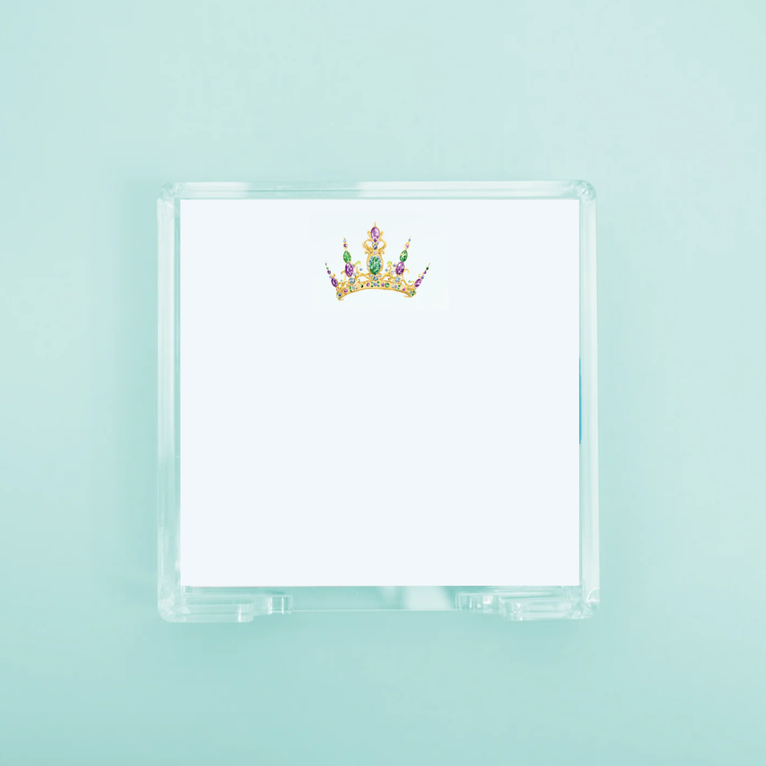 Illustration of a gold crown with vibrant purple and green jewels on a white notepad paper in a clear acrylic holder against a soft blue-green backdrop