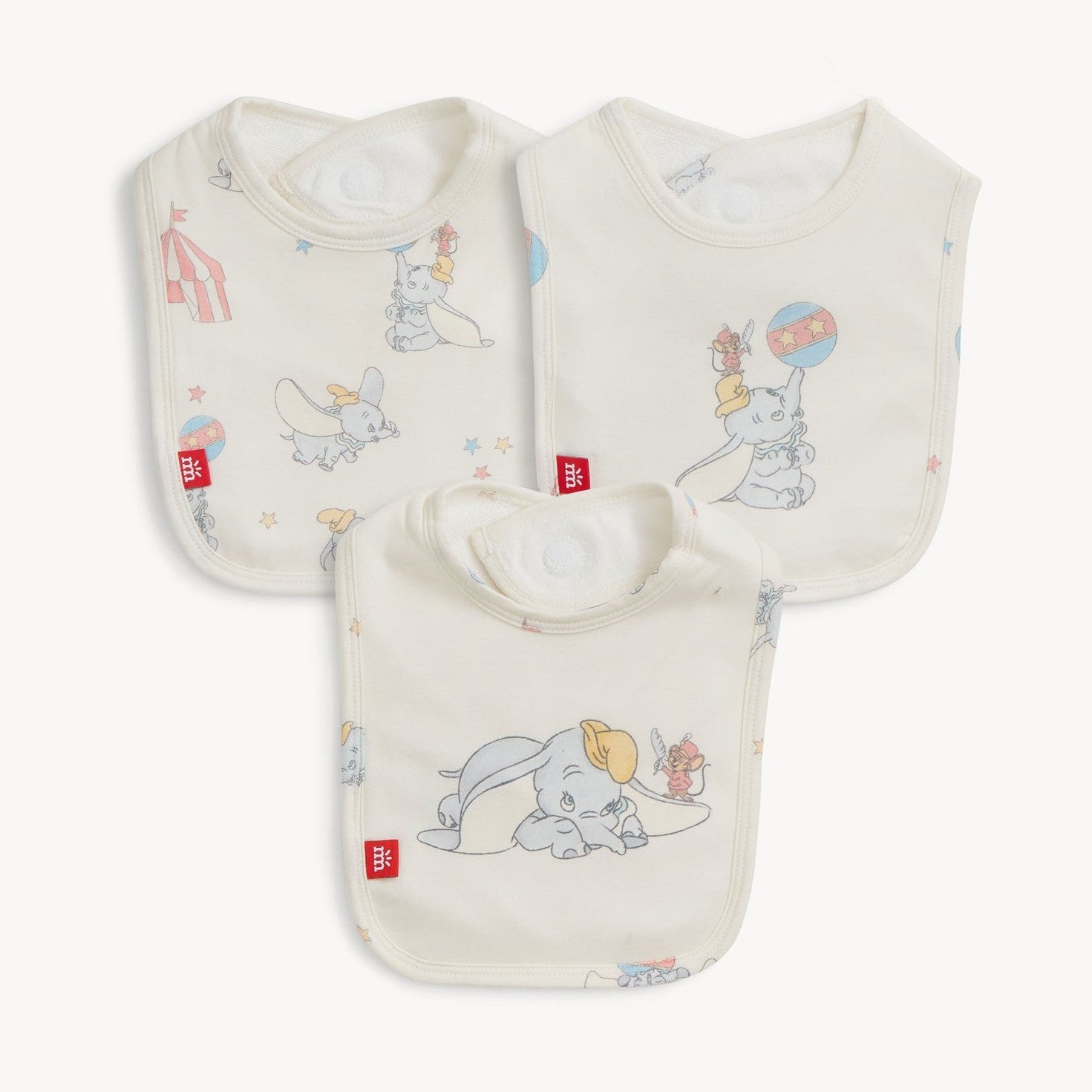 Three cream organic cotton baby bibs featuring pastel illustrations of Disney's Dumbo flying, sitting, and balancing a ball with Timothy Q. Mouse, surrounded by scattered stars and a circus tent design