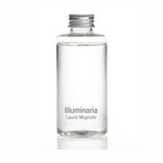 Product shot of a clear glass bottle with a silver screw cap, containing clear liquid and labeled Illuminaria Laurel Magnolia on a reflective white background