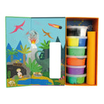 A children's dinosaur craft kit featuring an open illustrated box with a prehistoric scene including an erupting volcano, flying pterodactyls, and a fiery meteor, alongside neatly stacked containers of colorful modeling clay and an orange paper roll