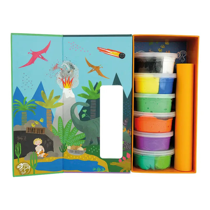 A children's dinosaur craft kit featuring an open illustrated box with a prehistoric scene including an erupting volcano, flying pterodactyls, and a fiery meteor, alongside neatly stacked containers of colorful modeling clay and an orange paper roll