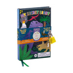 Children's "My Secret Diary" set featuring a dark blue cover with a vibrant prehistoric landscape including a purple Tyrannosaurus Rex, a red Pterodactyl, an erupting volcano, and a green palm tree, secured with a yellow padlock and keys, promoting "Includes Sticker Sheet" and "I Smell of Cola" scratch-and-sniff details