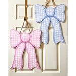 Painted wooden gingham bows, one pink and one blue, hanging by ribbons on a white paneled door