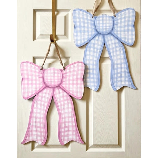 Painted wooden gingham bows, one pink and one blue, hanging by ribbons on a white paneled door
