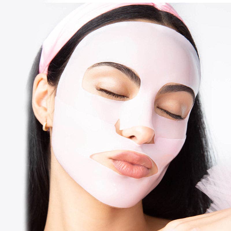 Photography of a woman with closed eyes wearing a light pink sheet face mask and a pink headband featuring a gold hoop earring