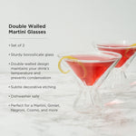 A pair of clear double-walled borosilicate martini glasses, each with subtle etched designs and filled with vibrant red cocktails garnished with yellow lemon peel twists, on a white marble surface