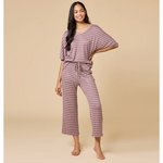 Photograph of a smiling woman modeling dusty rose and white striped loungewear in a studio featuring a V-neck top, cropped wide-leg pants with drawstring, and bare feet