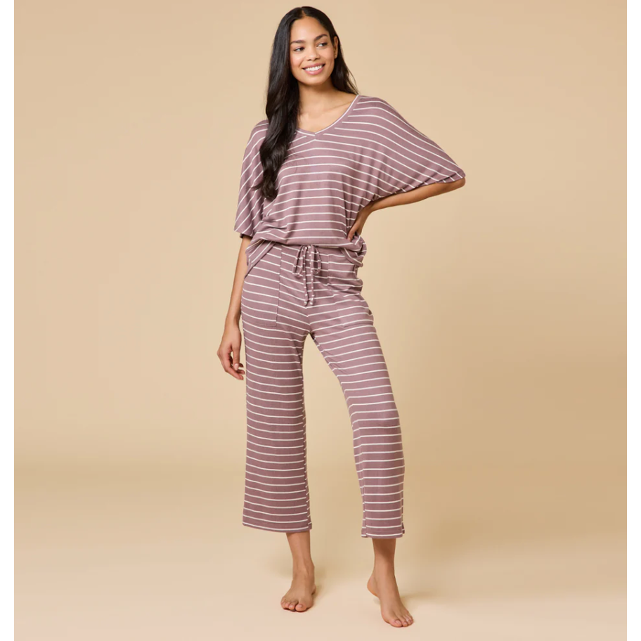 Photograph of a smiling woman modeling dusty rose and white striped loungewear in a studio featuring a V-neck top, cropped wide-leg pants with drawstring, and bare feet