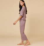 Smiling young woman with long dark hair modeling a dusty rose two-piece loungewear set with thin white horizontal stripes, walking barefoot in a studio