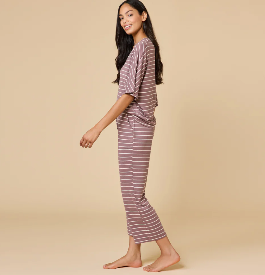 Smiling young woman with long dark hair modeling a dusty rose two-piece loungewear set with thin white horizontal stripes, walking barefoot in a studio