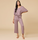 Studio photograph of a woman modeling a mauve and white horizontal striped loungewear set featuring a v-neck top and drawstring wide-leg pants against a neutral tan backdrop